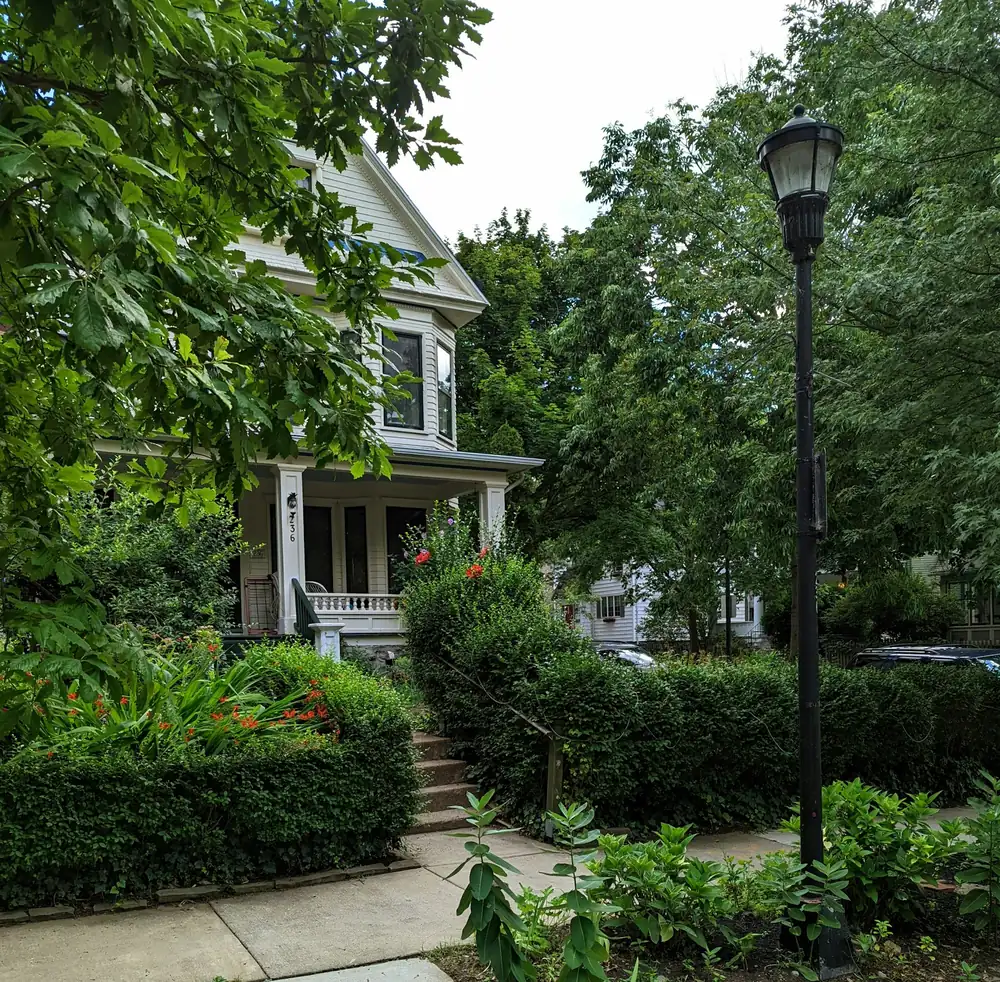 A Victorian house with a deep front porch behind a garden and an iron street lamp
