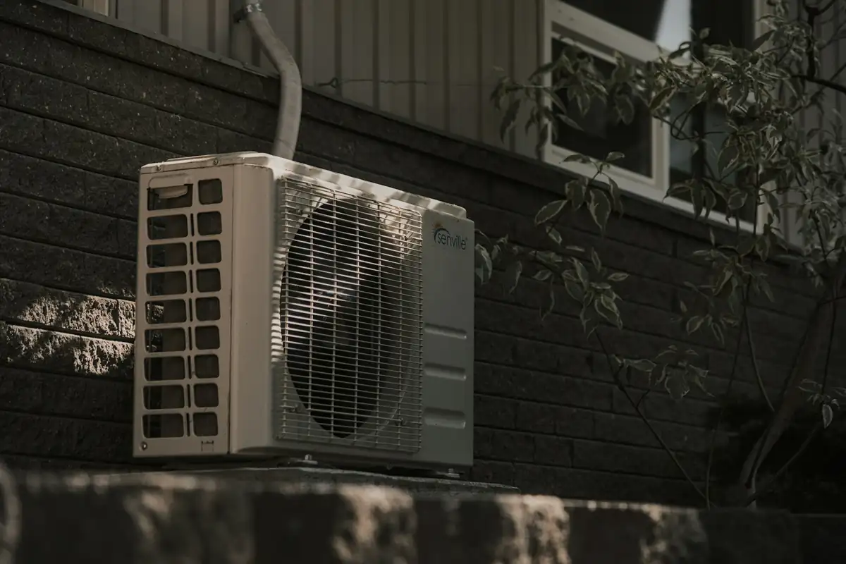 The outdoor unit of a ductless mini split on a ledge against a dark brick wall